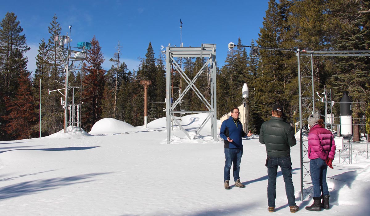 A scientist stands in a snowy forest talking to people